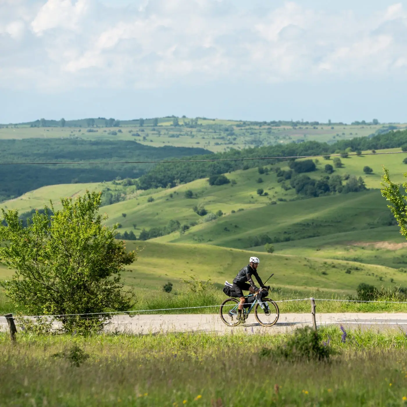 A bikepacker riding a quiet road above rolling green hills.