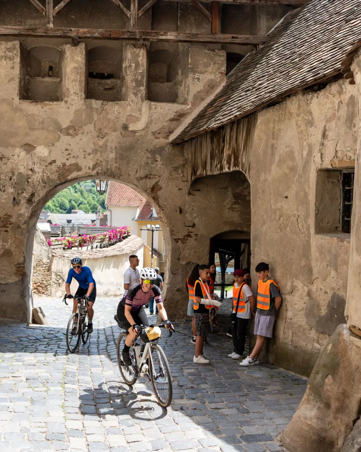 Two riders on cobbles under the timbered gate tower of Sighișoara citadel.